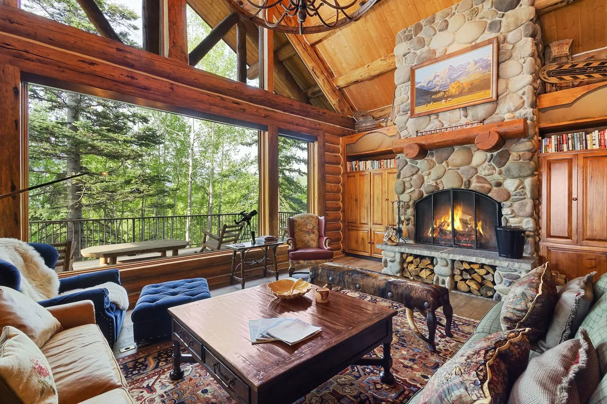 This image features an inviting great room with a dramatic stone fireplace as the focal point, flanked by large panoramic windows that offer sweeping views of the outdoors. The soaring vaulted ceilings are accented by exposed wooden beams, and plush seating is arranged for cozy gatherings.