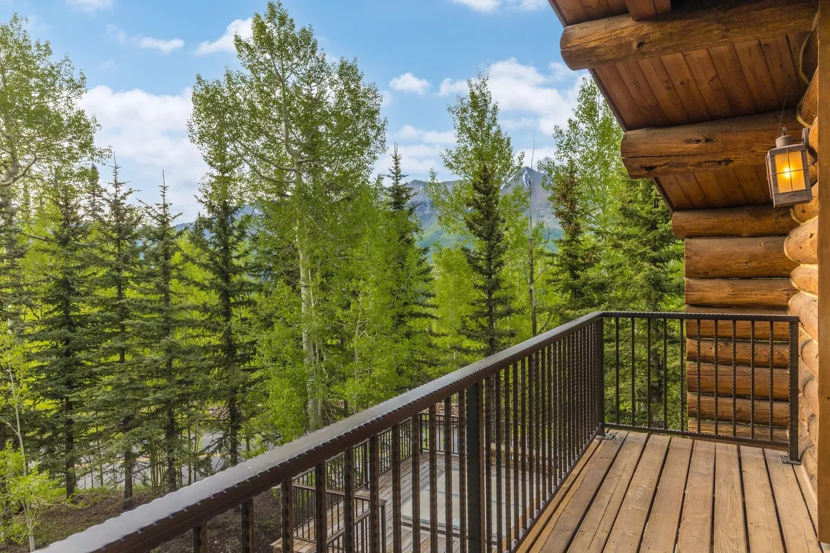 A peaceful cabin balcony with wooden railings overlooks lush greenery and distant mountains. Rocking chairs invite guests to relax, sip morning coffee, or enjoy an evening bonfire, with the warm glow of cabin lights suggesting coziness and connection.