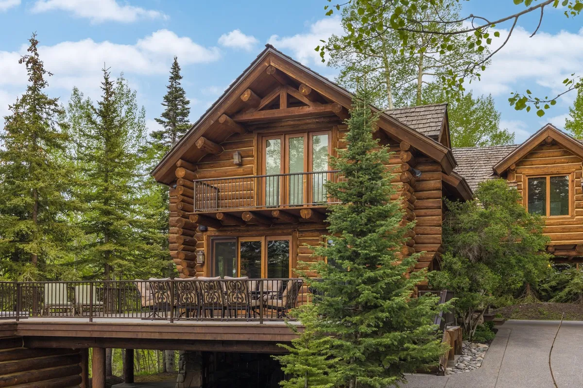 A cozy log cabin deck with comfortable seating overlooks surrounding trees, inviting guests to relax, dine outdoors, or enjoy scenic nature views. The atmosphere is peaceful and secluded, ideal for unwinding or sharing a meal with companions.