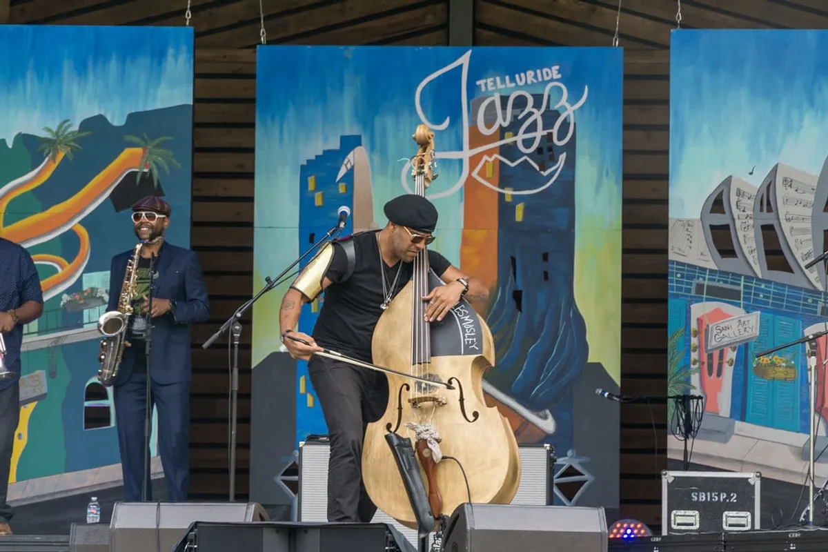 A lively outdoor music scene featuring musicians performing in front of a colorful mural. The audience mingles in a festive atmosphere, highlighting a joyful celebration of art and live music under the open sky.