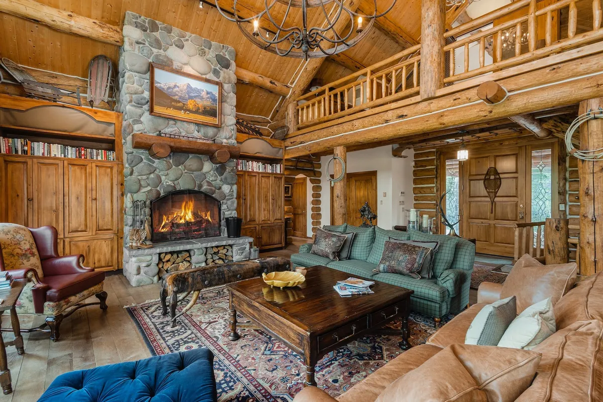 A warm, inviting great room with a large stone fireplace, rustic wooden beams, a cozy sitting area, and a coffee table. The atmosphere is perfect for gathering, enjoying hot chocolate, and recounting the day's mountain adventures.